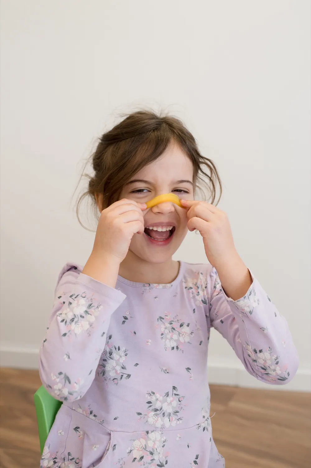 A laughing young girl holding a slice of yellow capsicum under her nose like a moustache