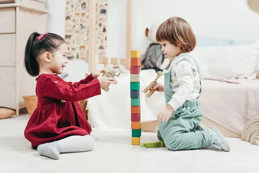 Two young children playing with wooden blocks and talking together