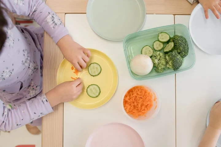 A child exploring cut cucumber, carrot and vegetables on colourful plates at the clinic