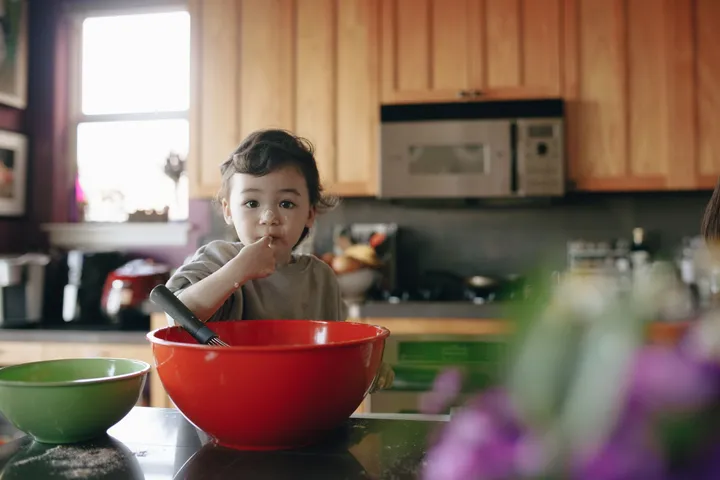 A toddler sitting at a kitchen bench playing with a large mixing bowl