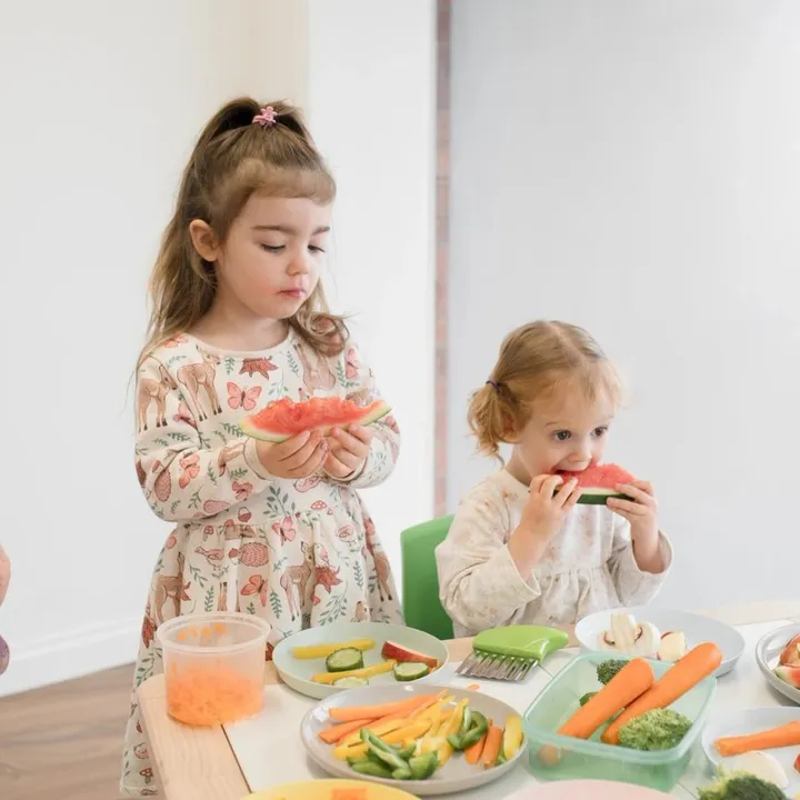 Two young children eating fruit and vegetables at a table during a feeding session