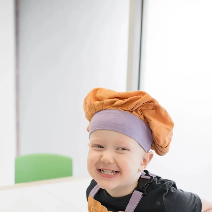 A young child smiling in a chef's hat during a playful feeding session