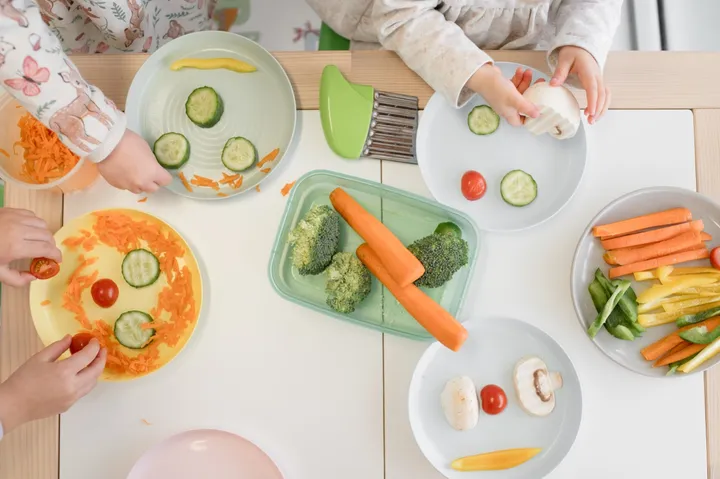 An overhead view of a table where children are making faces on their plates with carrot, cucumber and capsicum