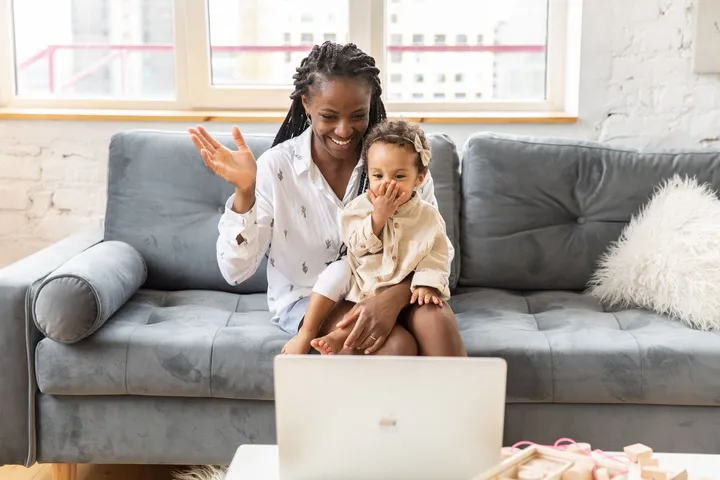 A parent and her young child smiling at a laptop during a video session at home